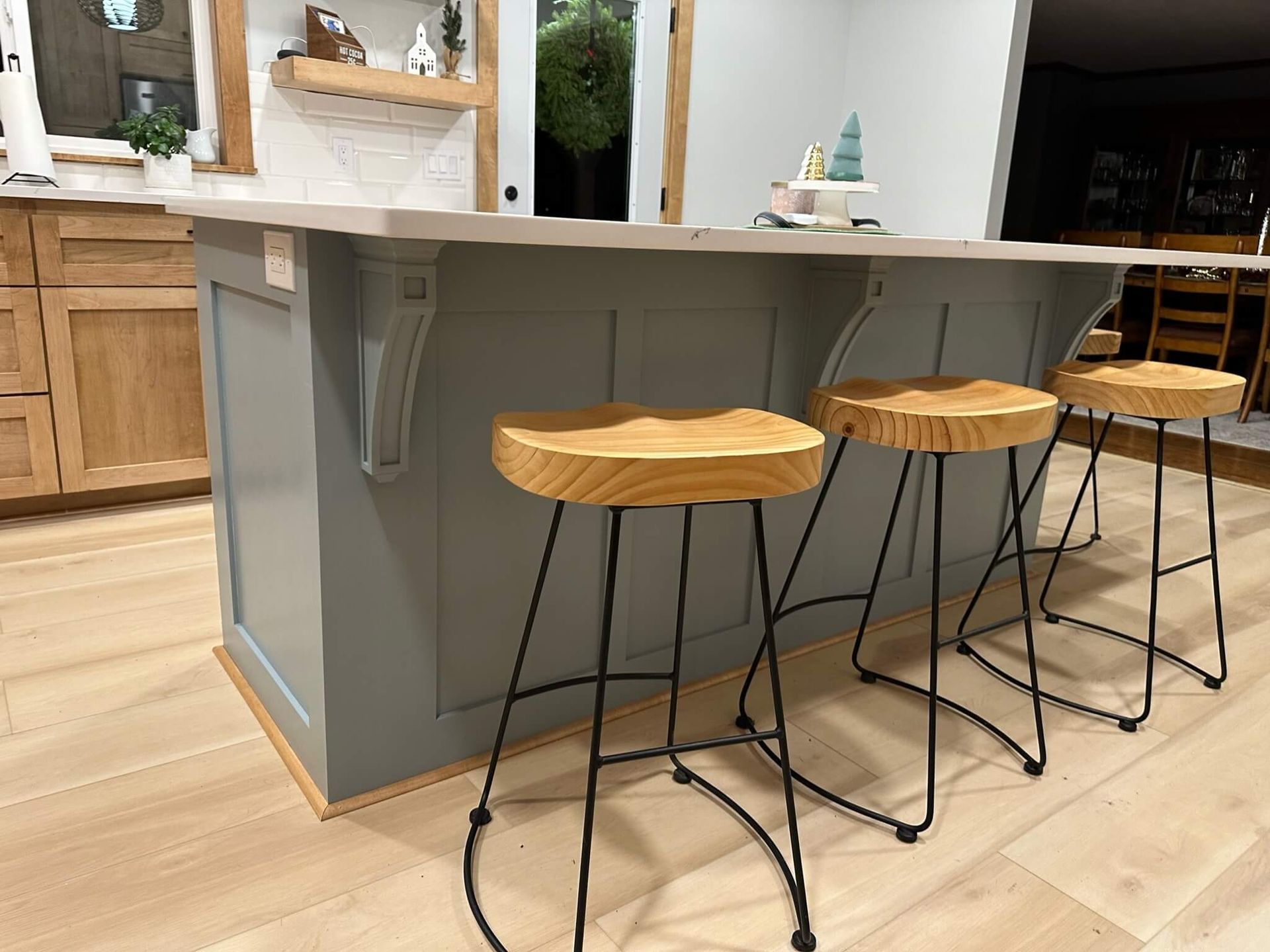 A kitchen island with blue-gray cabinets, wooden corbels, and a light countertop, featuring three wooden bar stools.