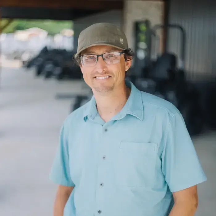 Smiling person in a light blue shirt and cap standing outdoors in a covered walkway