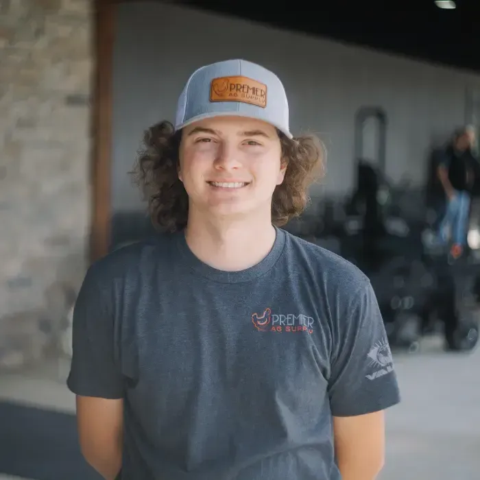 Smiling person in a gray T-shirt and blue cap standing indoors with bikes in the background
