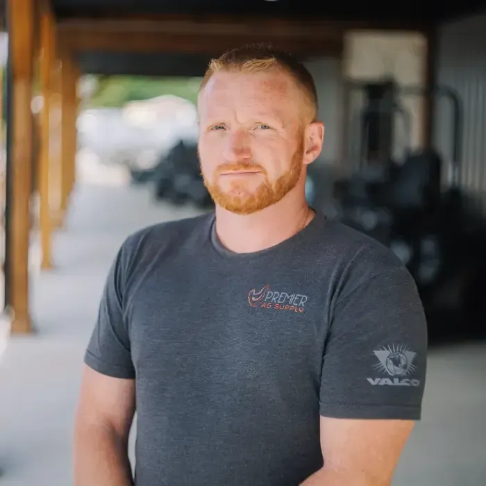 Man standing outdoors in a dark gray T-shirt, with a blurred industrial background.