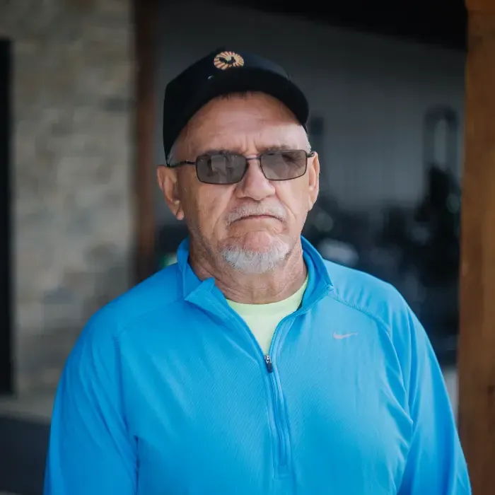 Man in black cap and glasses wearing a bright blue zip-up jacket, standing indoors with a neutral expression