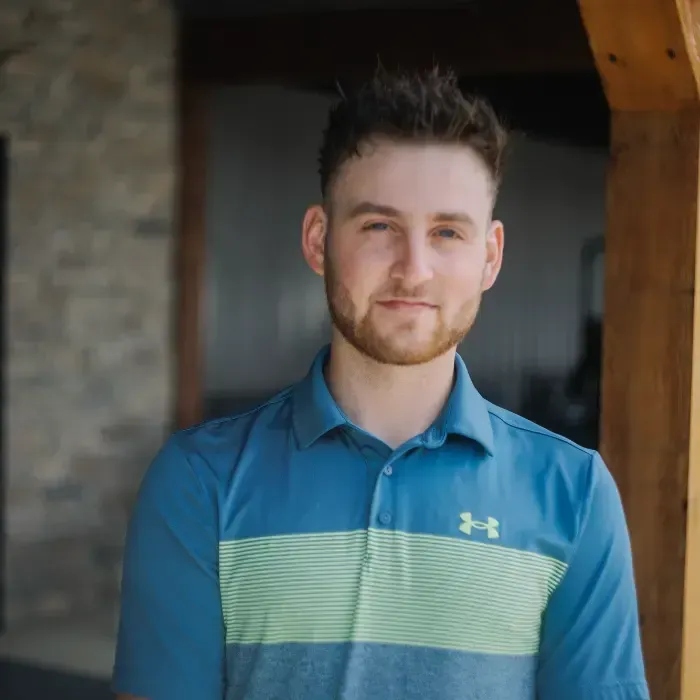 Man standing indoors in a blue collared shirt with a light green stripe, facing the camera.