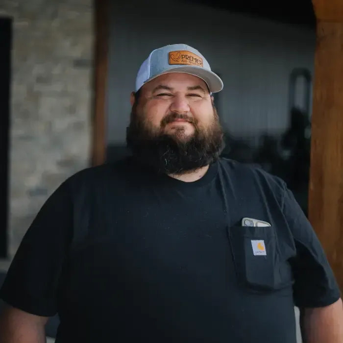 Smiling bearded man in a black shirt and gray cap standing outdoors by a doorway