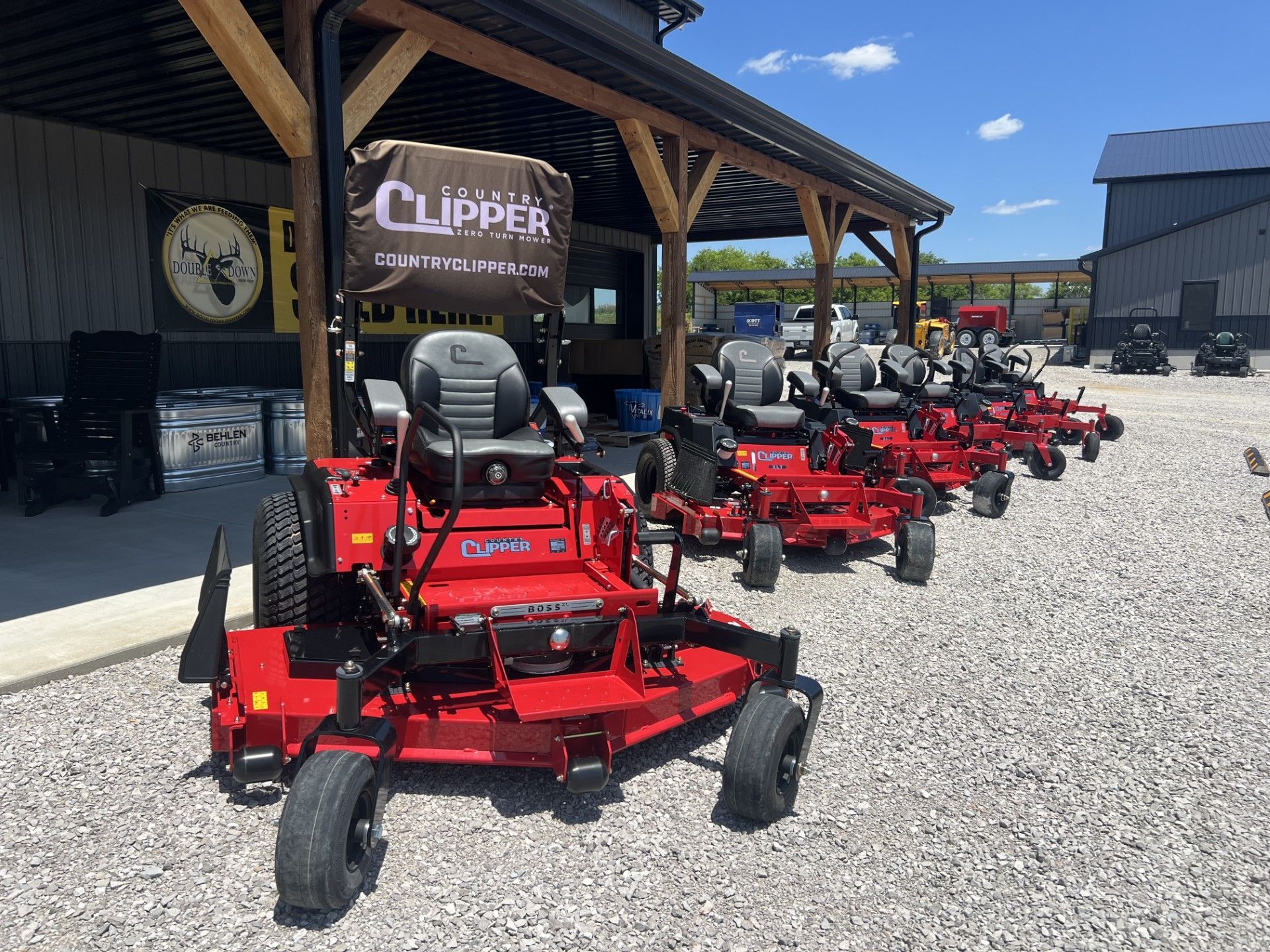 Row of red Clipper riding lawn mowers parked outside a dealership under a wooden awning