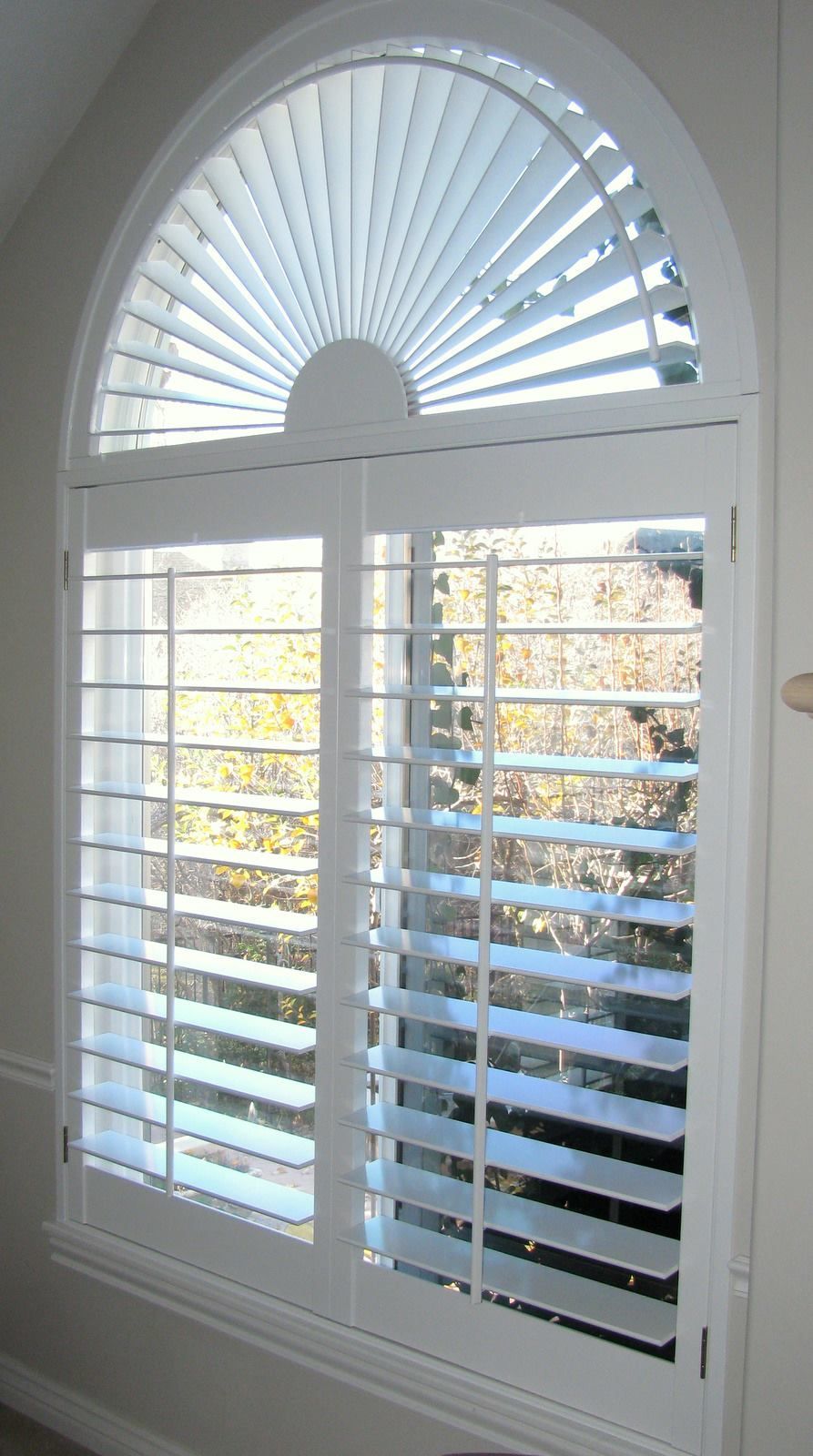 White shutters on arched window; sunlight streams through the slats.
