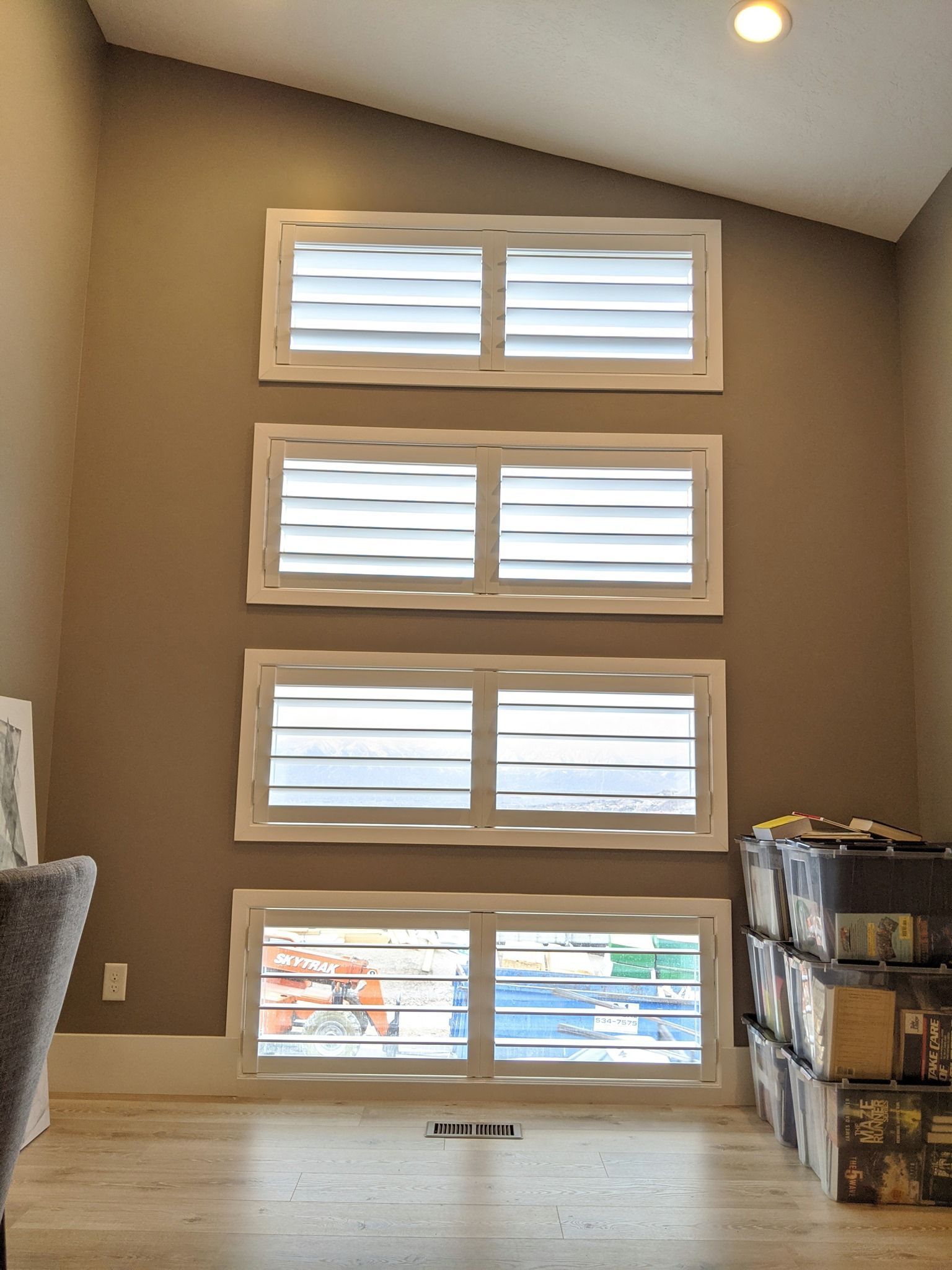 Four white-framed windows with open horizontal blinds on a tan wall in a room.