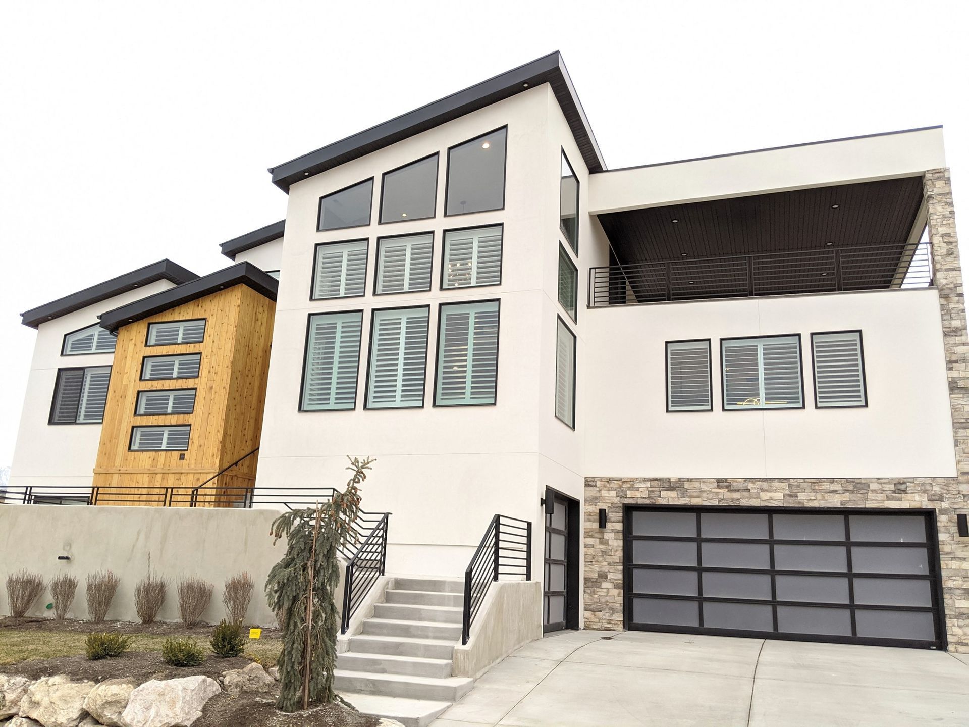 Modern white house with stone accents, glass garage door, and large windows.