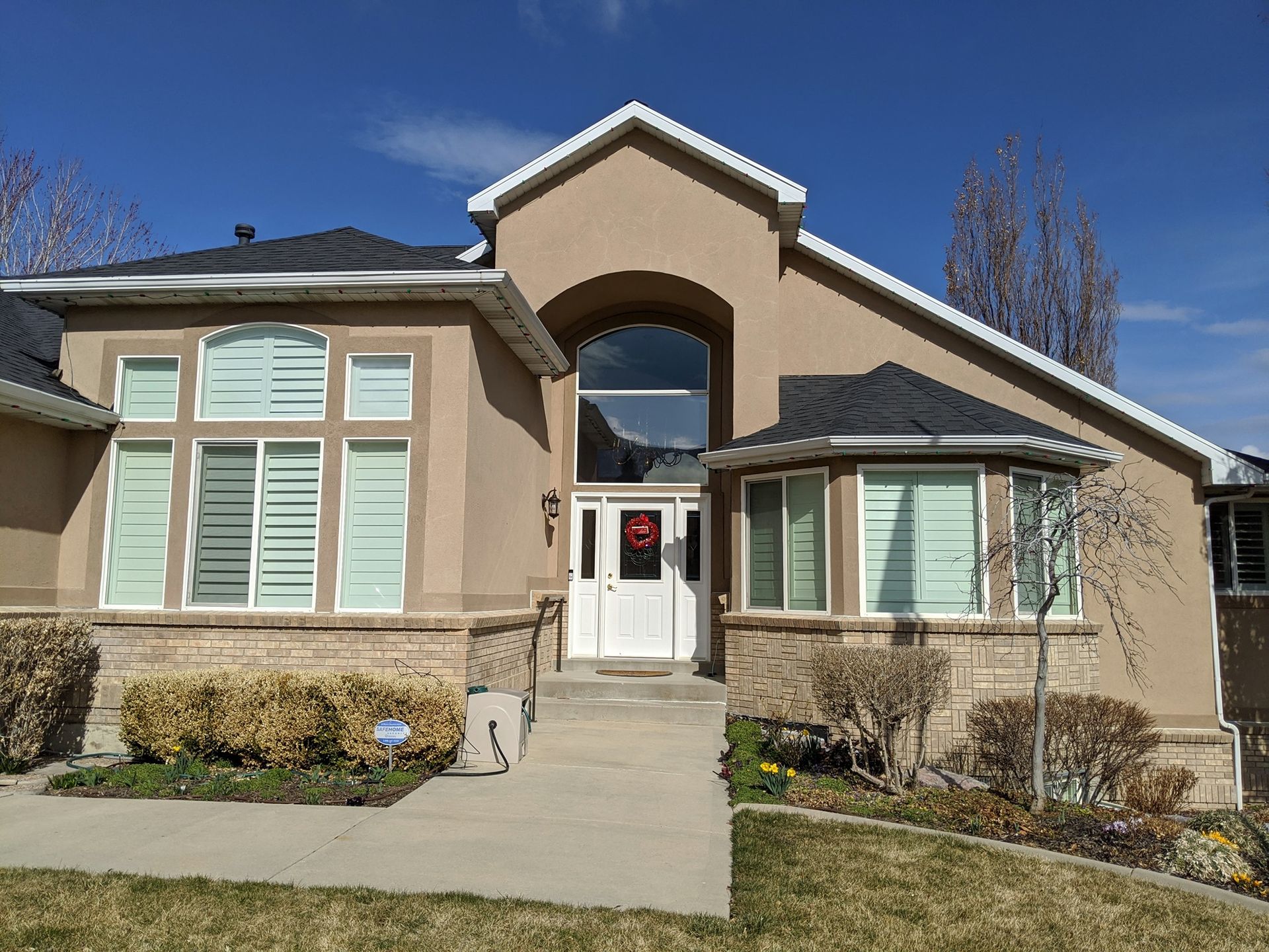 Tan stucco house with white trim, arched entryway, and blue sky.
