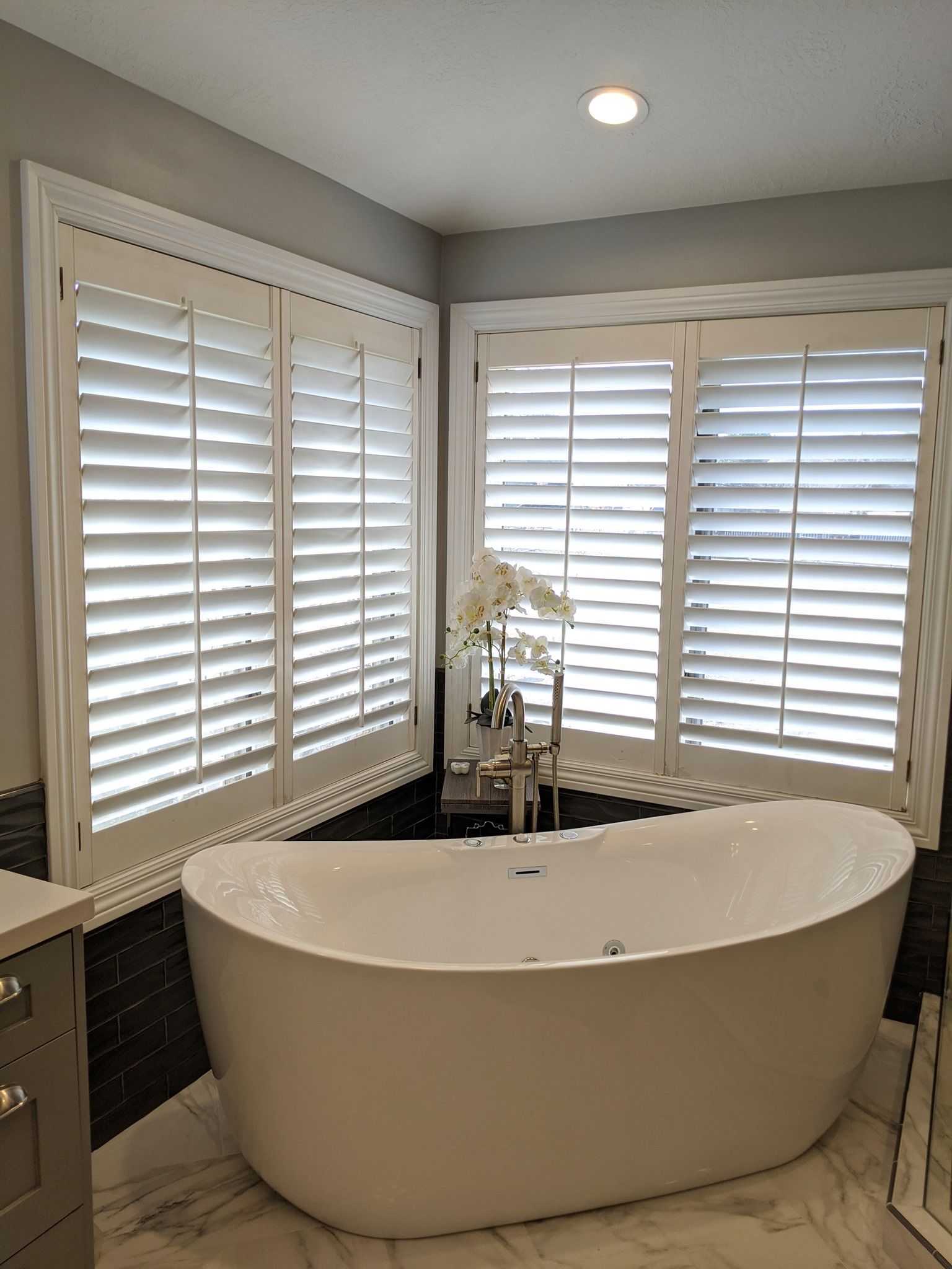 White soaking tub in a bathroom with white shutters on the windows.