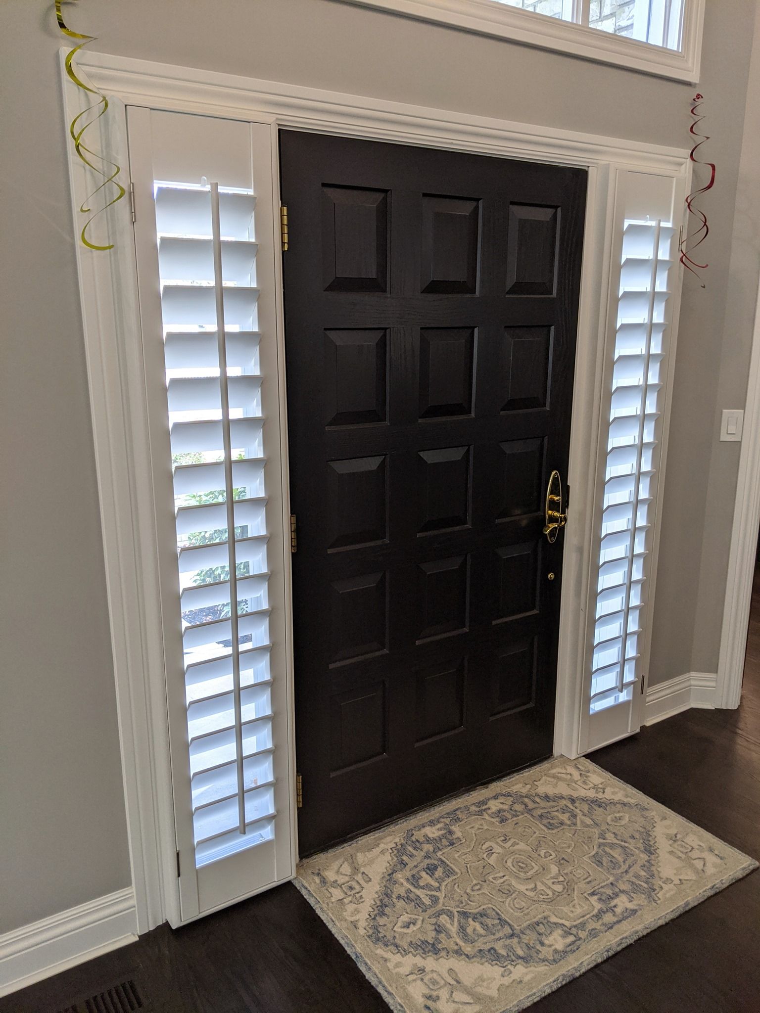 Black door with white shutters, topped with crown molding. A rug is in front of the door.