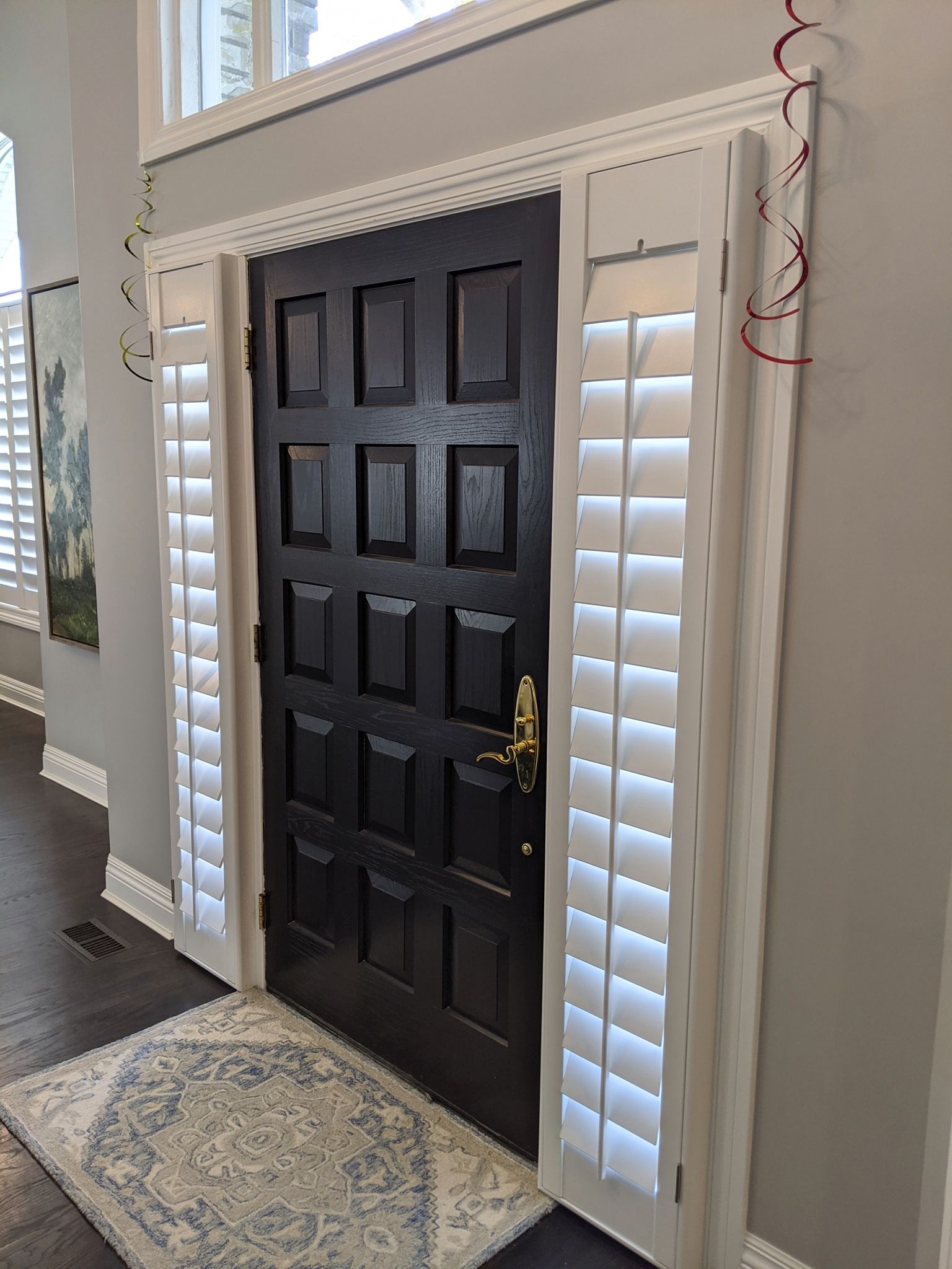 Black front door with white shutters and trim; a rug is in front of the door.
