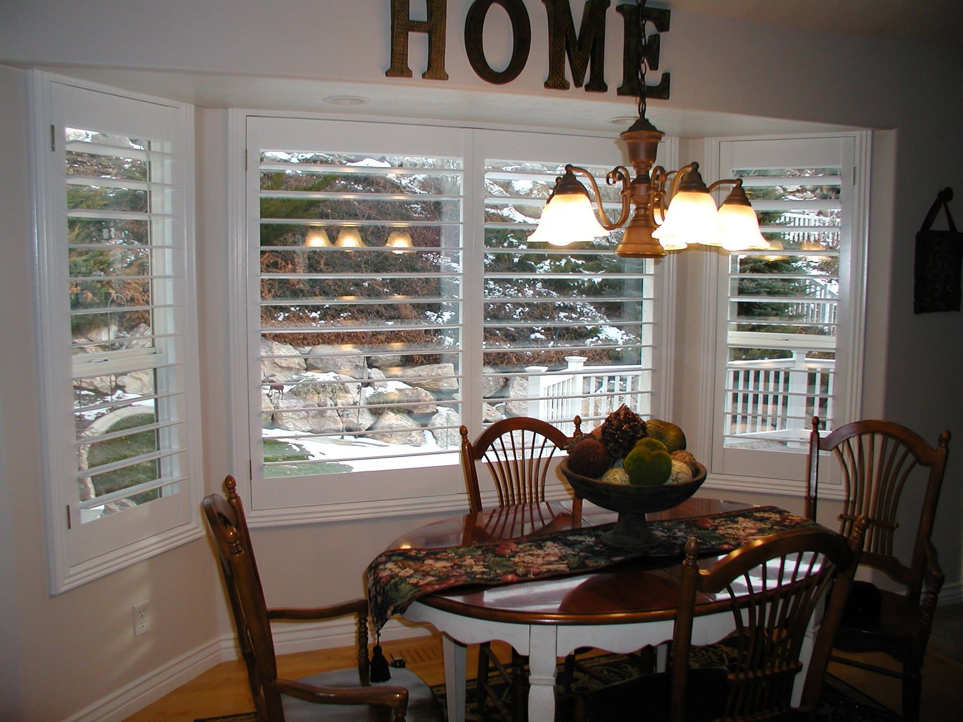 Dining area with bay windows, white shutters, and a round table set for a meal.