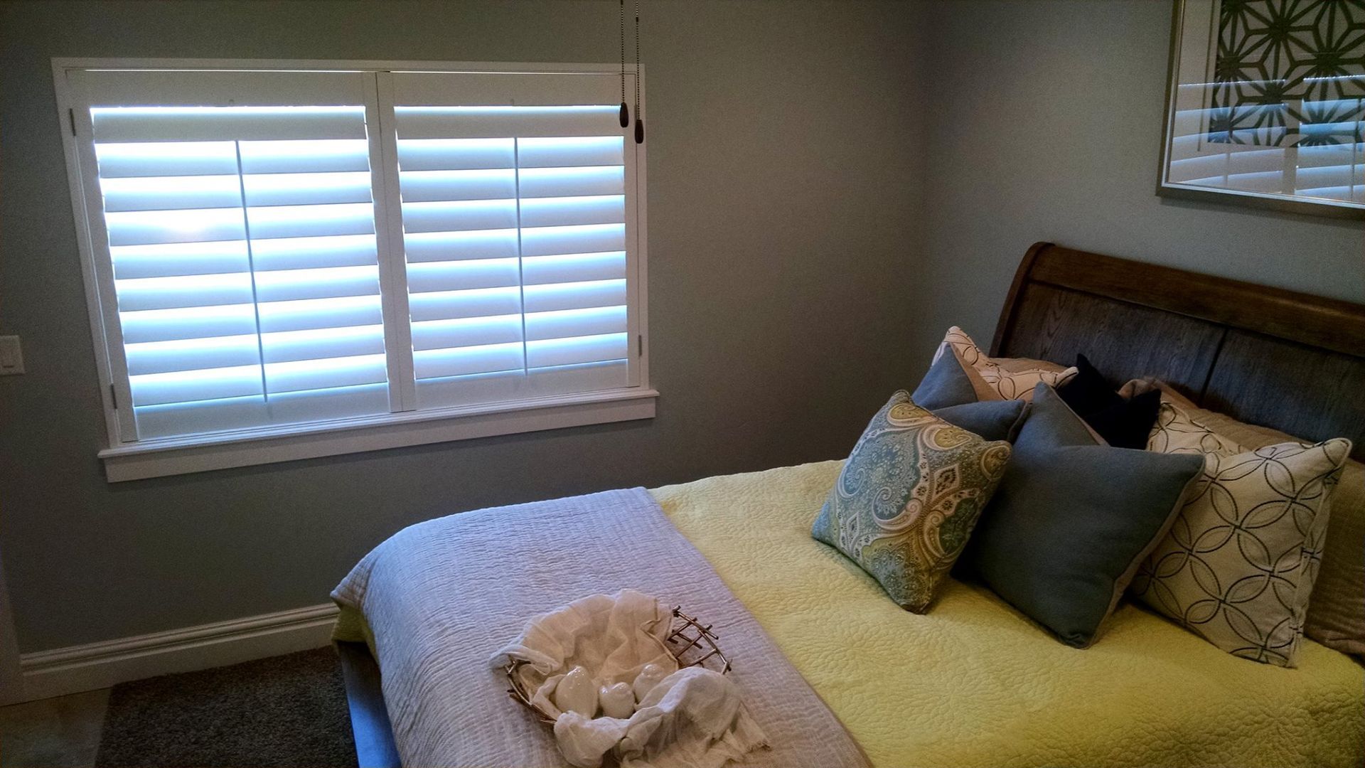 Bedroom with a bed, pillows, and a window with white shutters. The walls are gray.