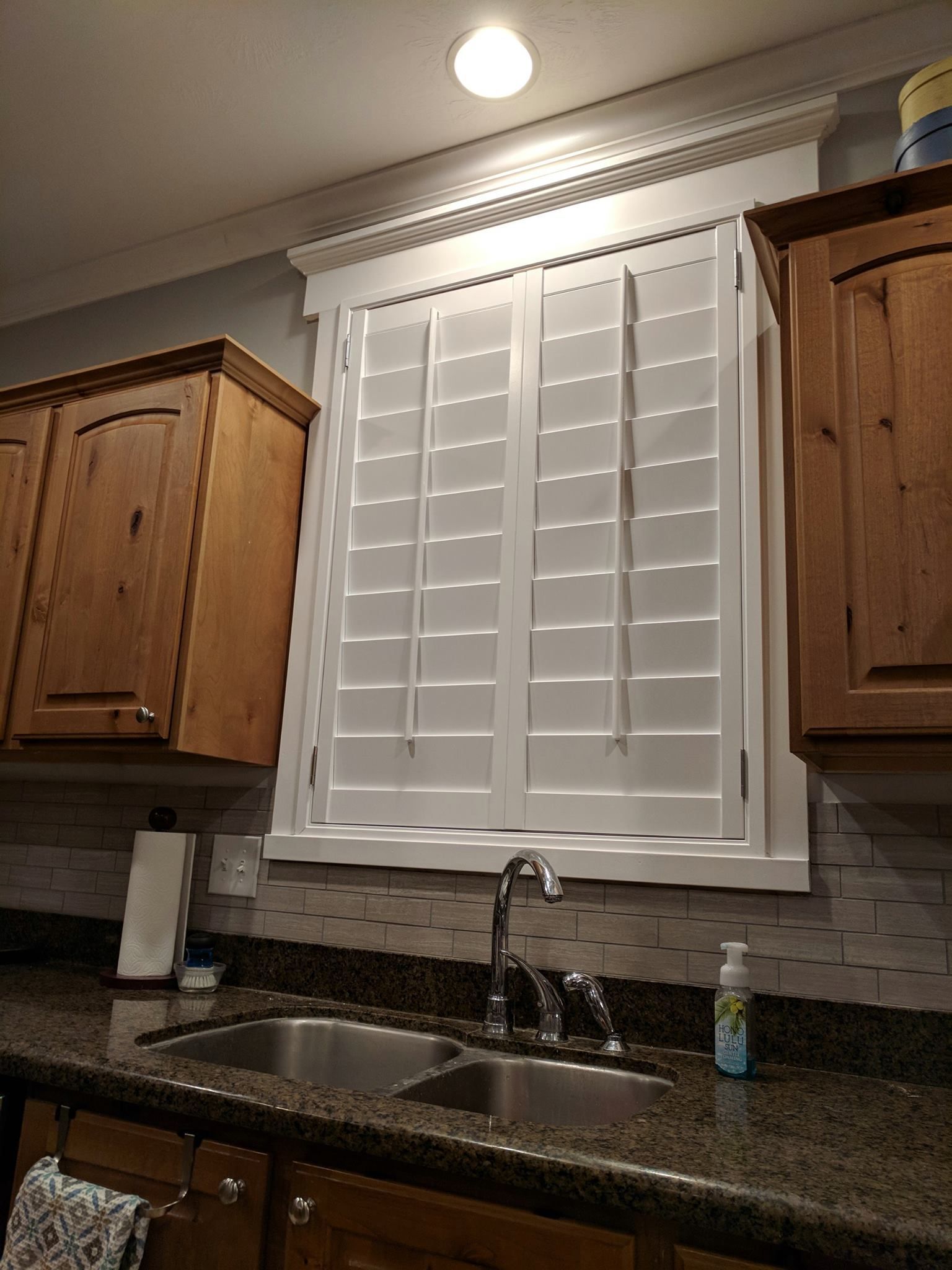 Kitchen with white shutters over a sink, brown cabinets, and a granite countertop.