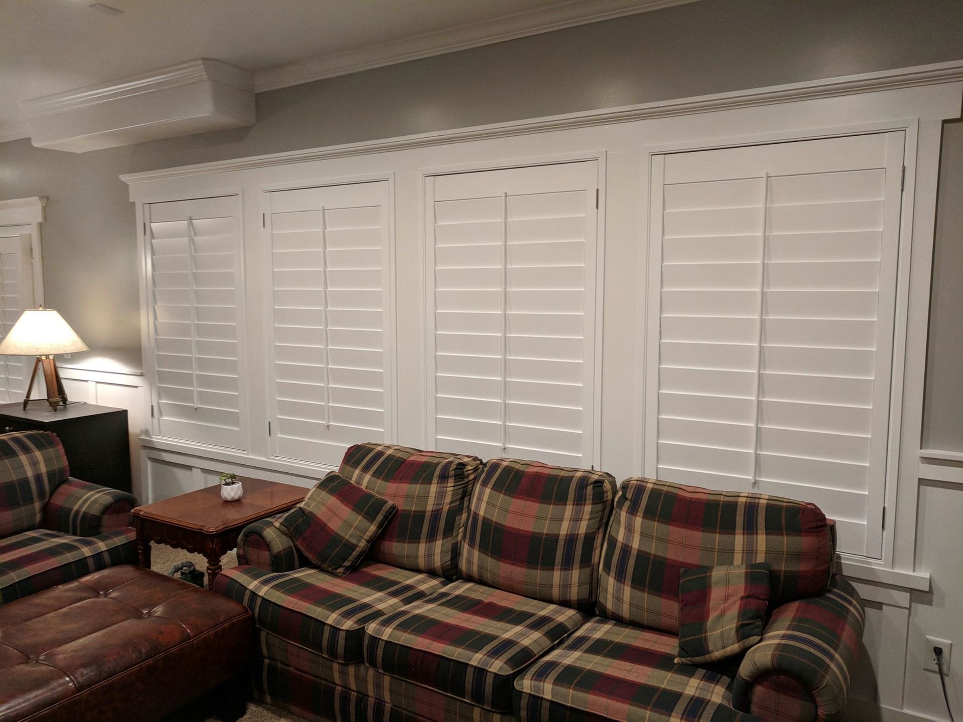 Living room with plaid couch, white shutters, and a small table with a lamp.