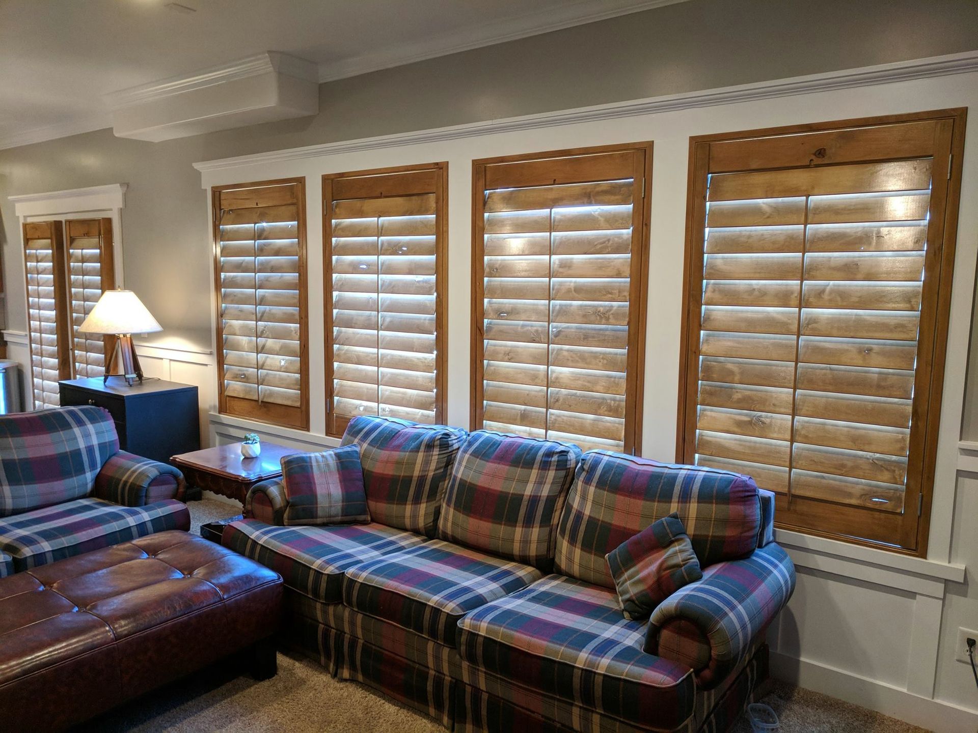 Living room with plaid couch and armchair, wooden shutters, and a lamp.