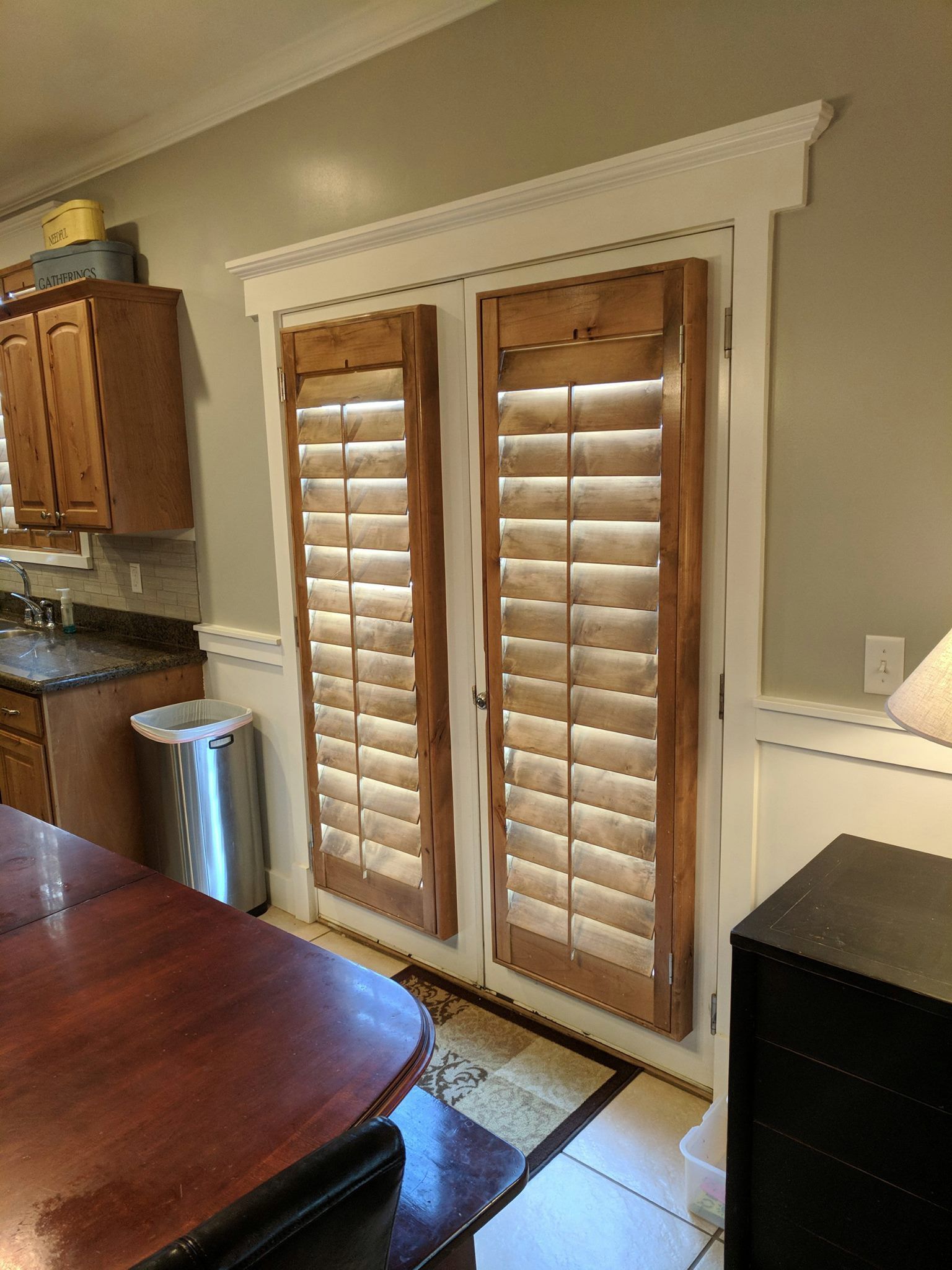 Wooden shuttered doors with white trim in a kitchen, with a table in the foreground.