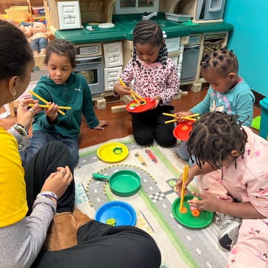 A group of children are sitting on the floor playing with plates and chopsticks