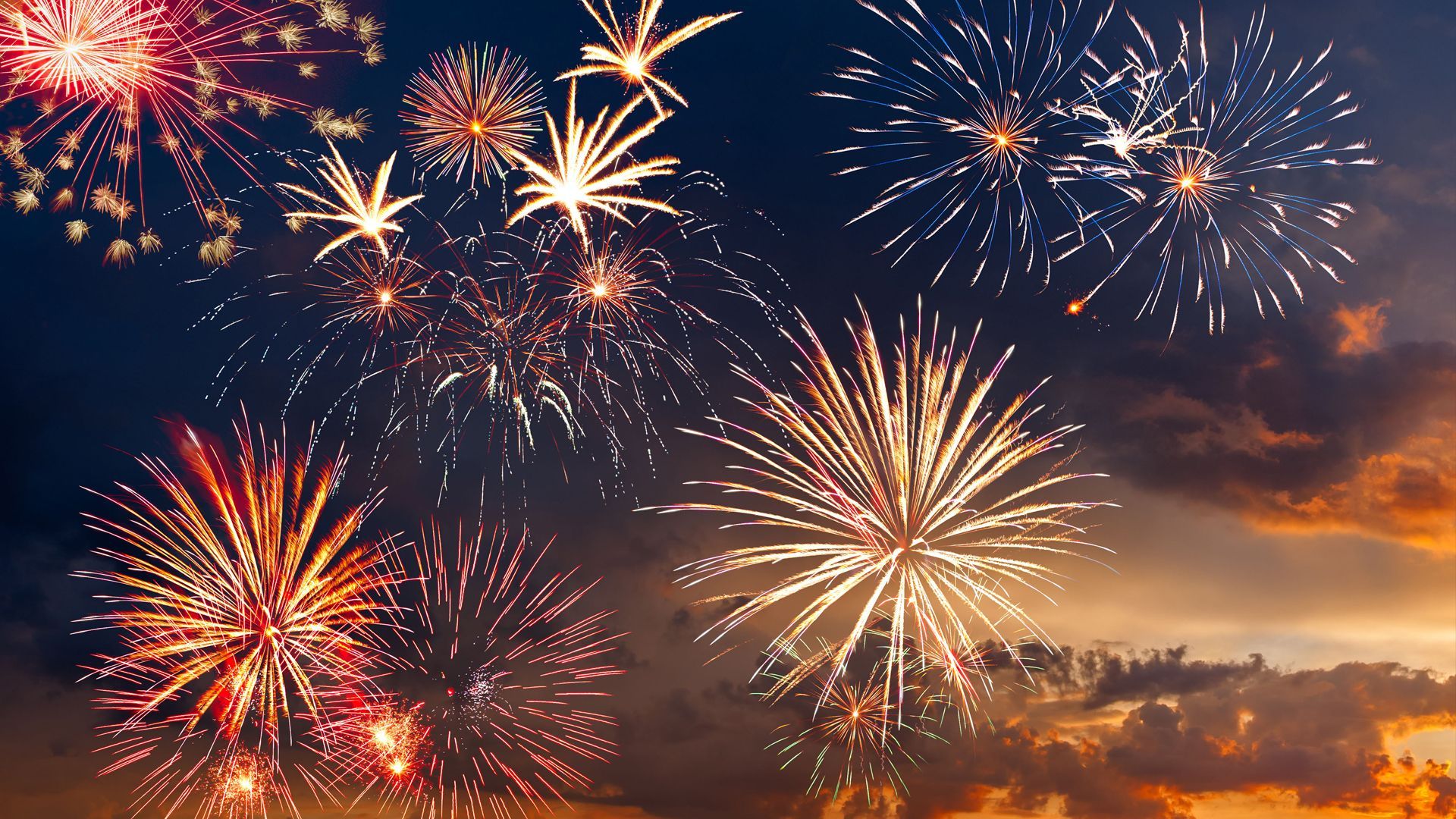 A bunch of fireworks are flying in the sky at sunset.