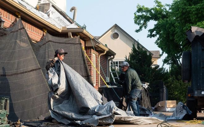 Two workers installing tarp on a brick building, setting sun.