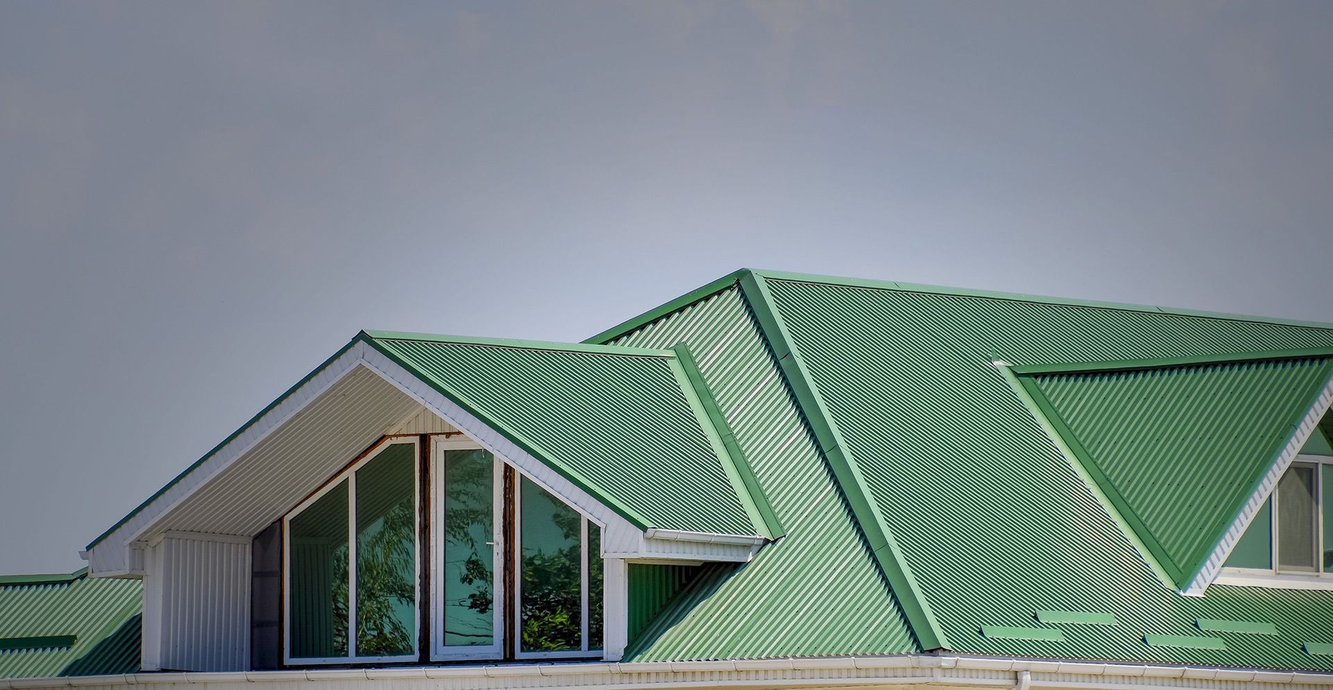 Green metal roof on a white house, with triangular gables and large windows.