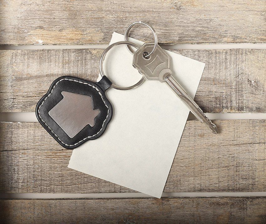 Keys and house-shaped keyring rest on a wooden surface beside a blank white card.
