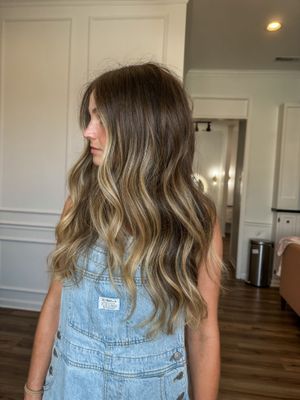 A woman with long hair is standing in a room wearing overalls.