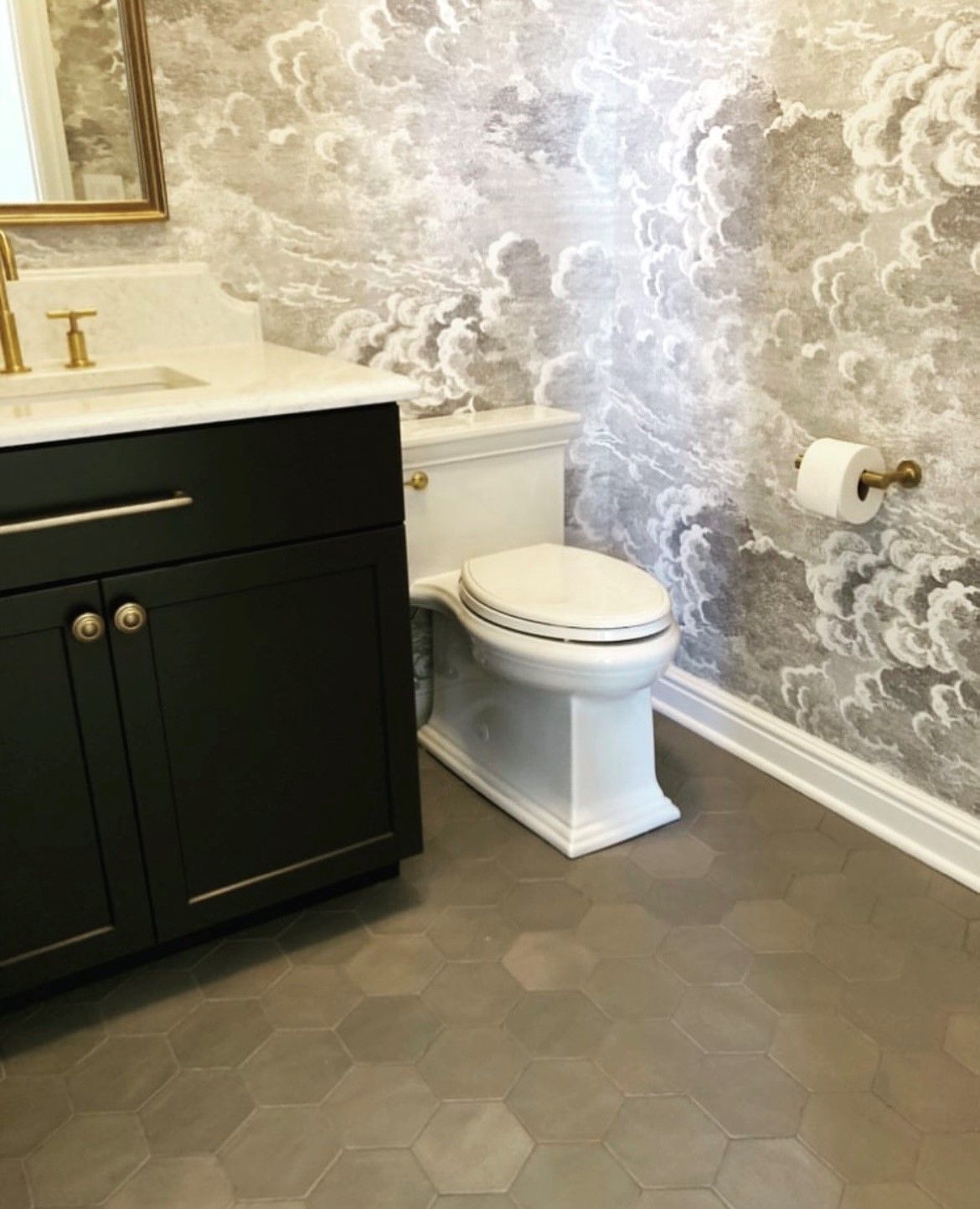 A bathroom with a toilet, sink, mirror and cloud wallpaper