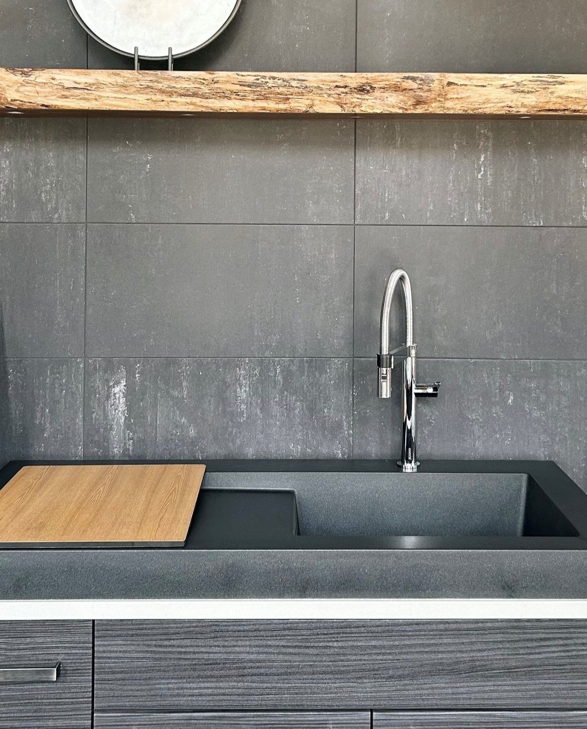 A kitchen sink with a wooden cutting board underneath it