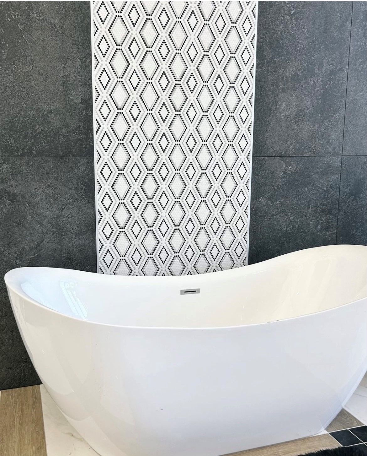 A white bathtub is sitting in front of a black and white tile wall