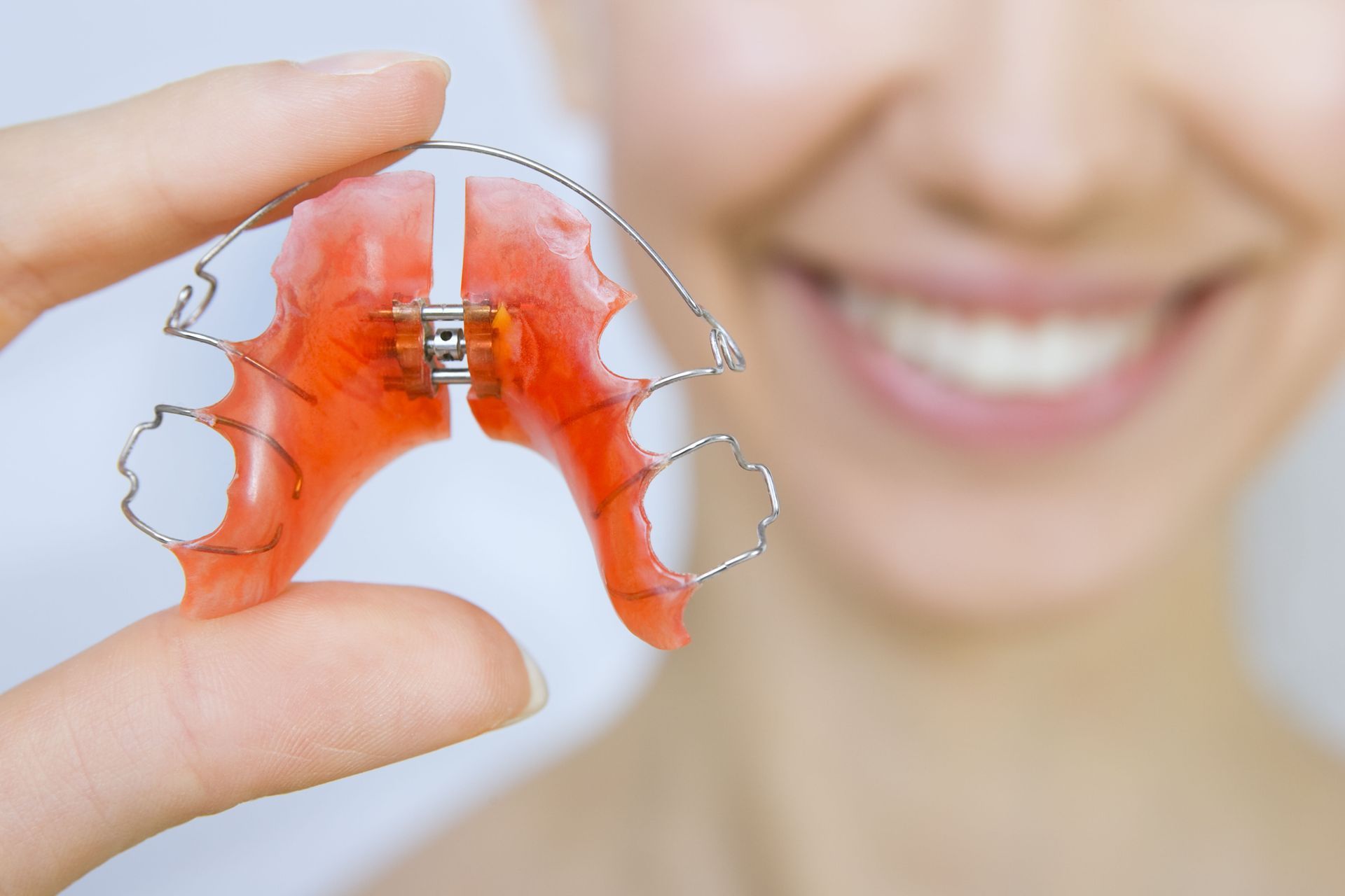 Woman holding a red and silver dental retainer, smiling with clear teeth.