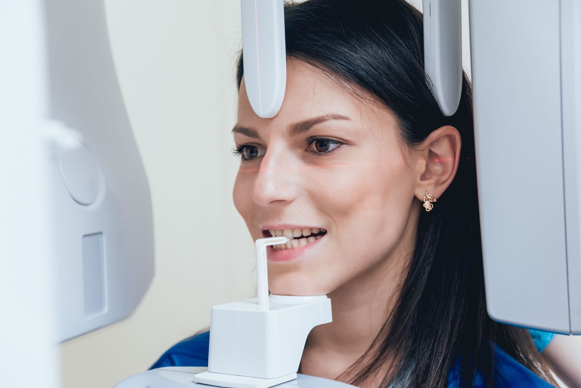 Woman having dental X-ray, head in machine, smiling with white fixtures.