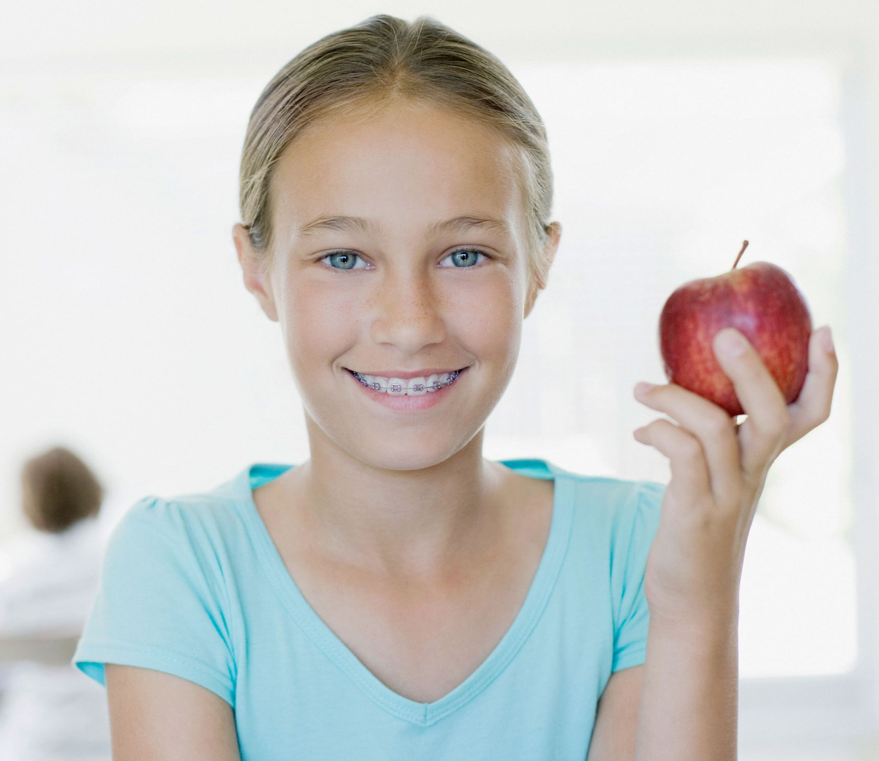 Girl with braces smiles, holding a red apple.