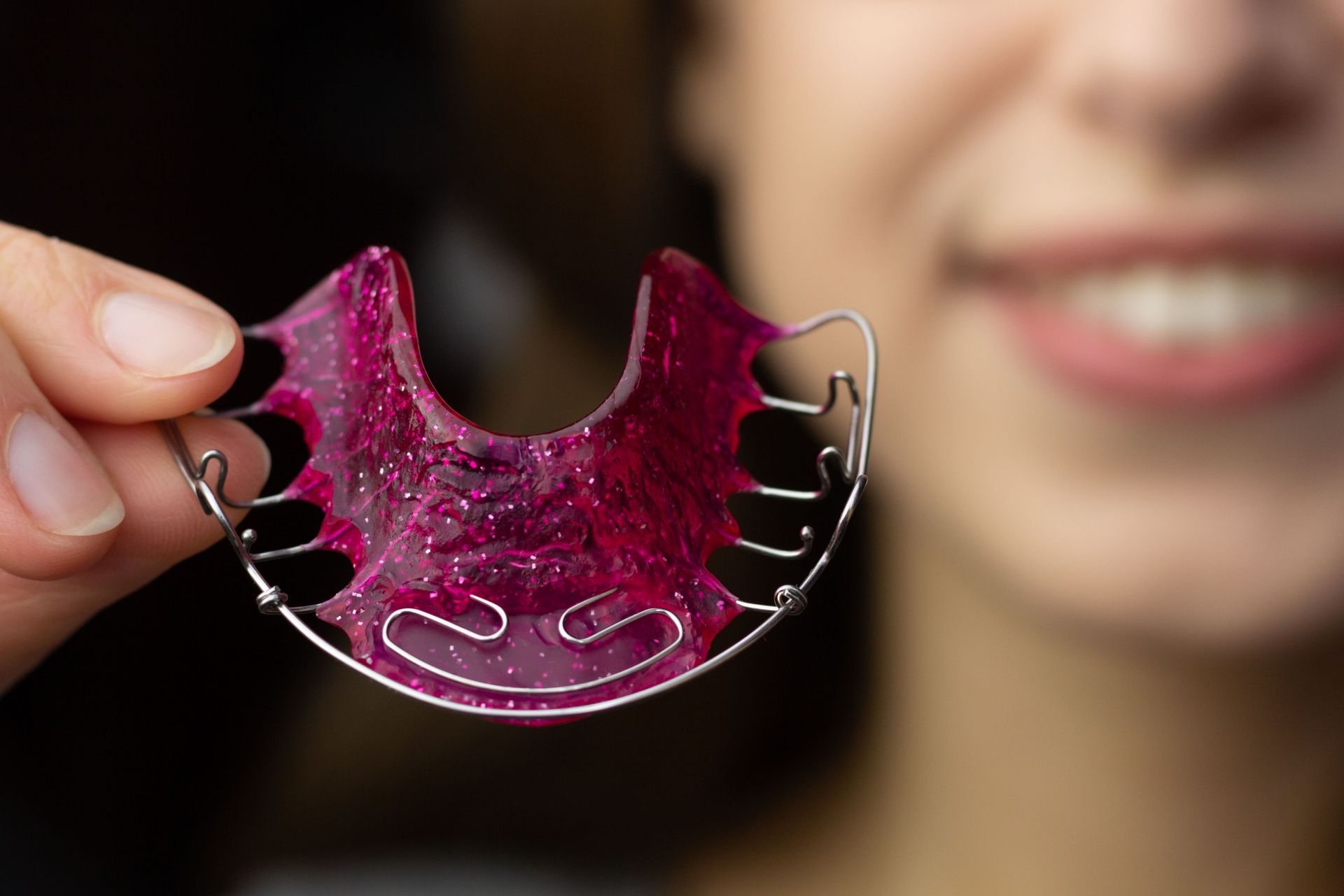 Person smiling, holding a pink and glittery orthodontic retainer.