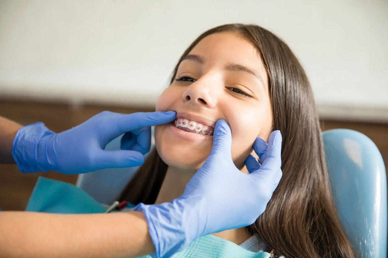 Dentist examining a patient's braces. The patient smiles in a dental chair.