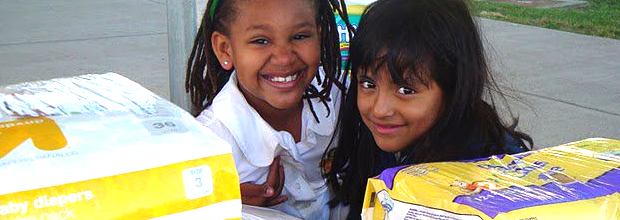 Children smiling in front of donated diapers