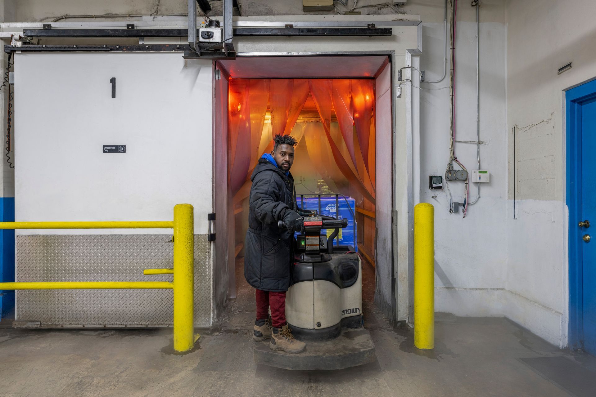 A man is driving a forklift through a door in a warehouse.