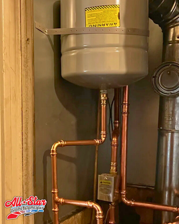 A light grey expansion tank mounted to a wall above new copper plumbing pipes and a small electrical box.