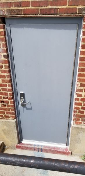 A gray door with a silver handle set in a brick wall.