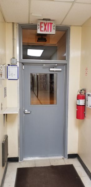 A gray door with an exit sign above it, fire extinguisher to the right.