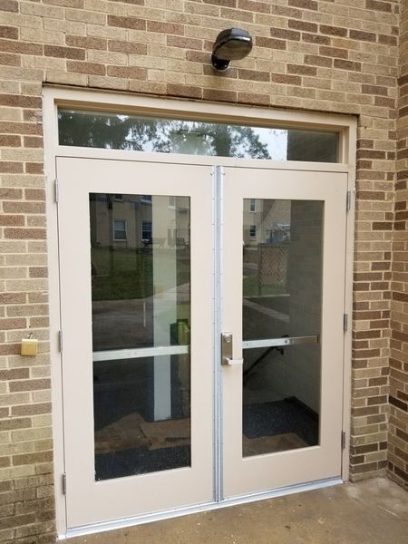 Double glass doors with a cream-colored frame and a small window above, set in a brick wall.