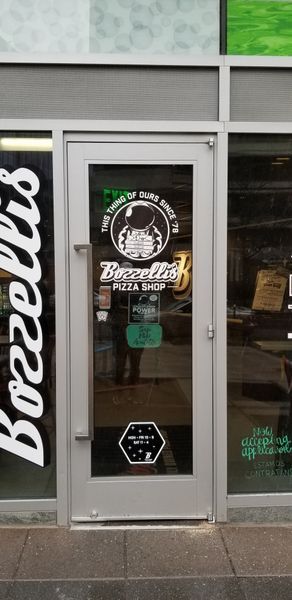 Bozzelis Pizza Shop storefront with a glass door displaying the restaurant's logo.