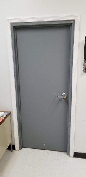 A closed, gray door with a silver handle in a room with white walls and trim.