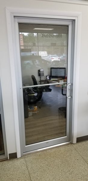 Glass door into an office with a desk, chair, and computer visible through it.
