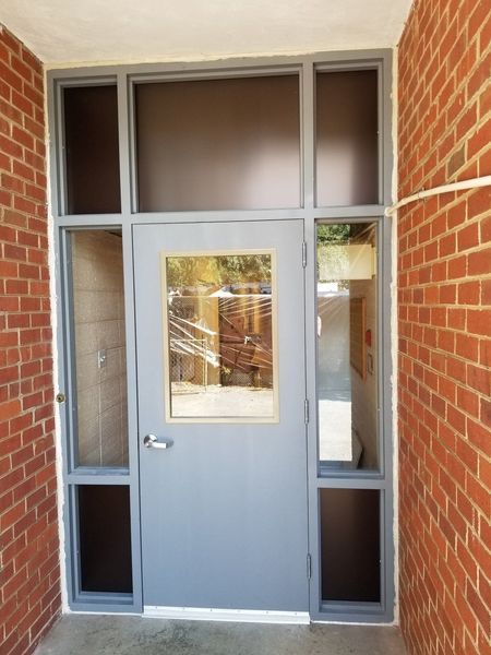 Gray door with glass panel, surrounded by glass windows, set in a brick doorway.