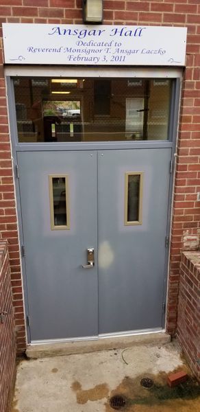 Gray double doors with rectangular windows, leading into Ansgar Hall, brick building.
