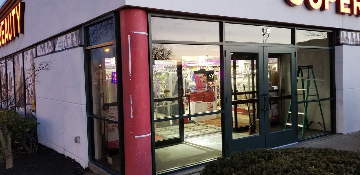 Exterior of a business with glass doors and windows, featuring a red support column and a ladder inside.