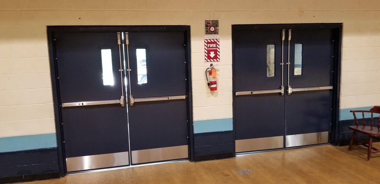 Two navy double doors with silver trim and bars. A fire extinguisher and signage are to the right.