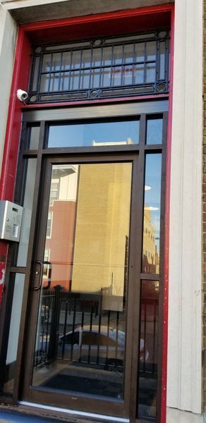 Exterior door with security bars and a red and brown frame.  A reflection of buildings can be seen in the glass.