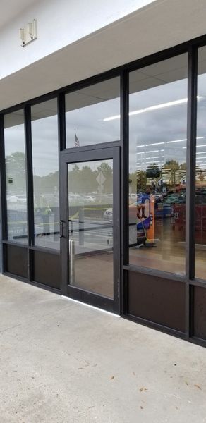 Exterior view of a commercial storefront with glass windows and a door reflecting the outdoors.